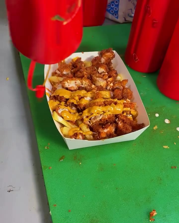Red sauce being squeezed over a tray of crispy chicken on the truck's green counter